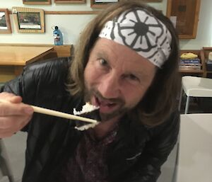 A man eats a sushi roll with chopsticks