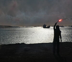 A person holding a flare waving farewell to a ship on the ocean.