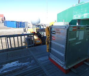 A yellow jcb telehandler (vehicle) putting a large grey metal box onto metal decking