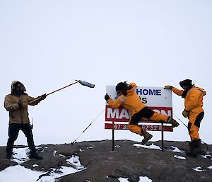 Three people in yellow outdoor gear are standing near a sign as they are filmed for a film festival