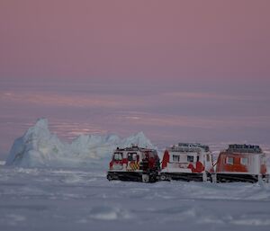 Three red vehicles sit on the snow in soft pink light