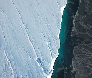 An aerial shot looking down on the edge of an iceberg with a small section of green water visible