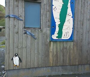 A painted sign with a map of Macquarie Island hangs on an outside wall of a wooden building