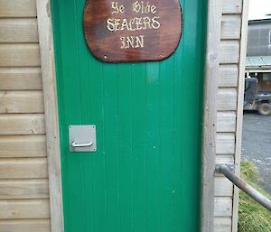 A wooden sign hangs on an green outside door