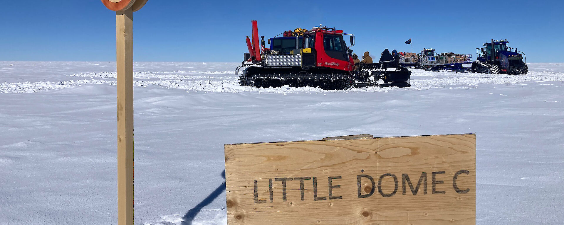 Two vehicles sit on the snow with a sign saying Little Dome C