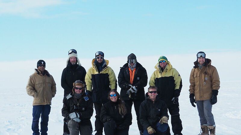 A team of people in cold weather gear stand on the snow