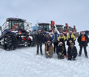 A team of people in Christmas hats stand on the snow in front of large machinery