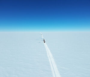 An aerial shot of tractors in the snow against a bright blue sky