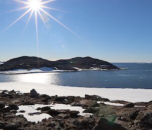 View from a rocky hill of an island in the bay, with the sun high overhead on a cloudless day.