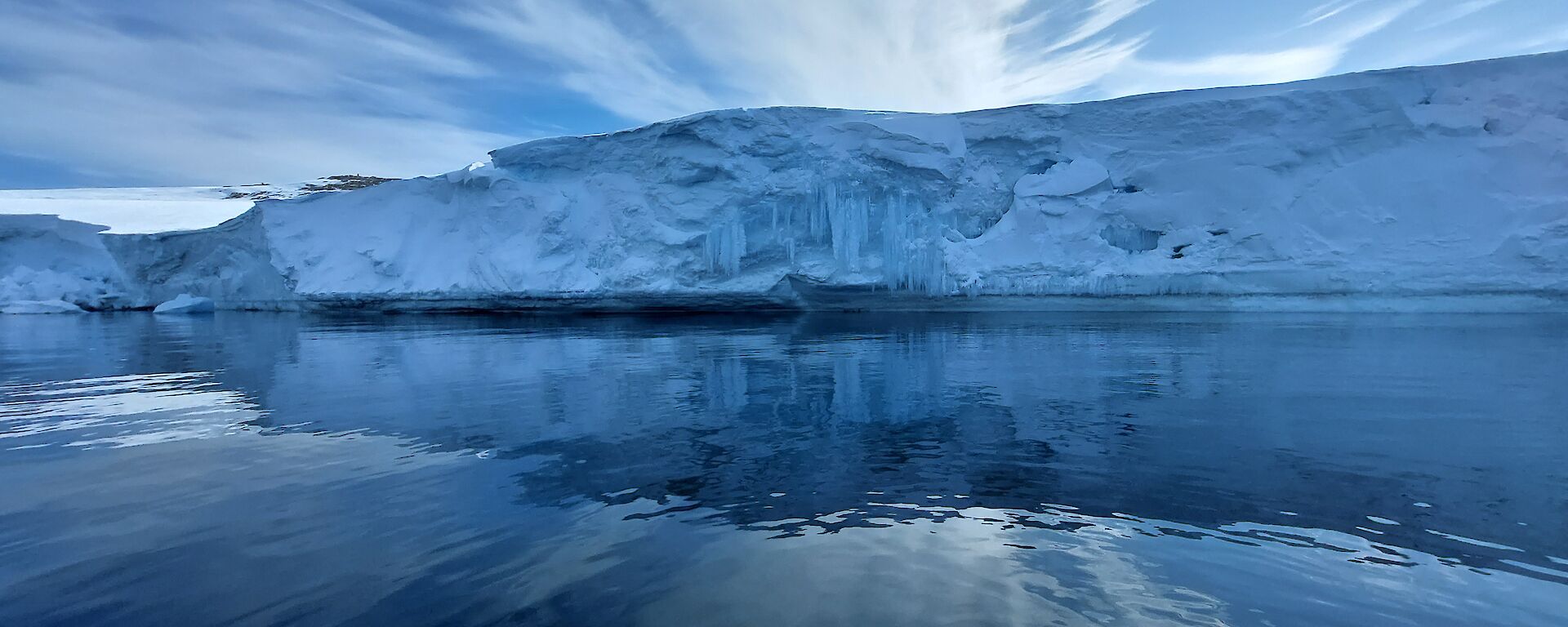 Tall ice cliff with frozen waterfall over-hanging on the bay, with ocean in the foreground.