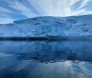 Tall ice cliff with frozen waterfall over-hanging on the bay, with ocean in the foreground.