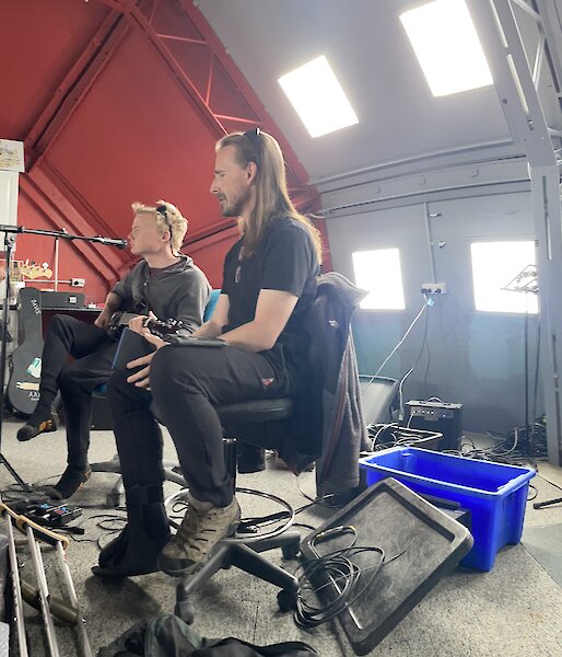 A group of musicians practicing on their instruments including drums, electric guitars, and an acoustic guitar.
