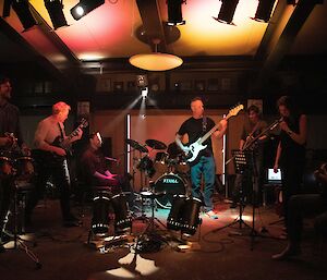 A band playing musical instruments. It is dark and they are lit up by colourful lights.