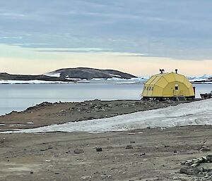 A yellow building sitting in an icy landscape with the ocean in the background. The building looks like a half cylinder lying on its side.