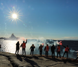 People standing on the shore farewell a ship as it heads into the sun