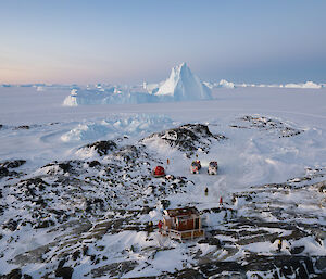 An aerial view of a red hut in the field surrounded by rocks and distant icebergs