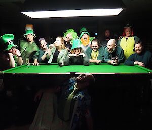 People dressed in green pose over a green pool table