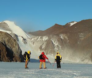 Three people stand on the snow in front of rock cliffs