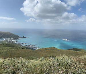 View from the top of a grassy hill shows a cruise ship in the blue water below