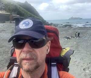 A man with a back pack stands on the shore with a cruise ship on the horizon