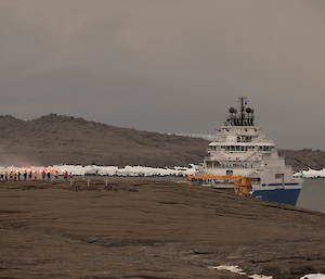 A group of people standing on shore farewell a blue and white ship