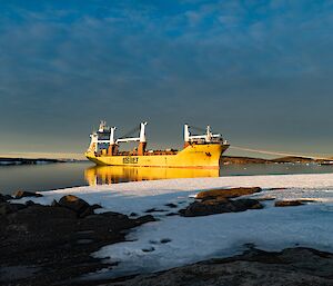 A yellow ship is moored in harbour