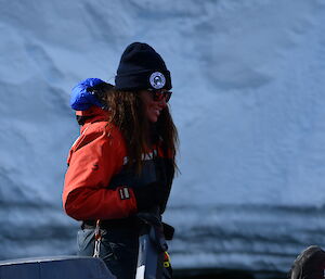 A smiling woman holding a boat tiller with an ice cliff in the background.