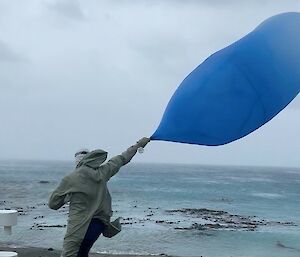A person holds a large blue balloon in the wind