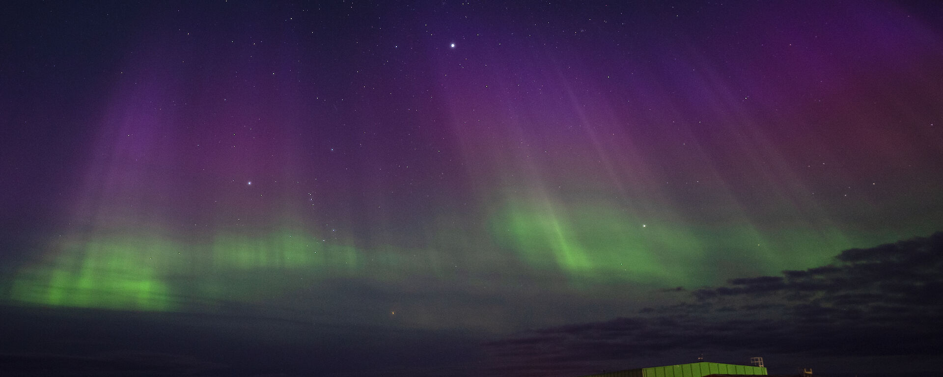 An aurora shines in green and purples over station buildings
