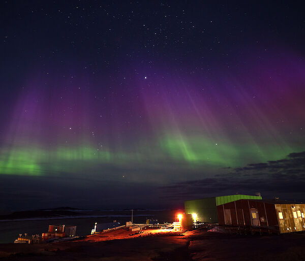 An aurora shines in green and purples over station buildings