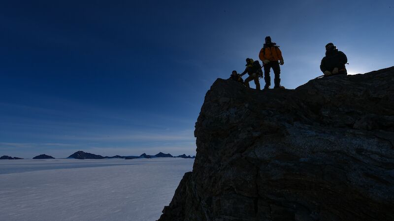 Three expeditioners silhouetted against the night sky atop a mountain