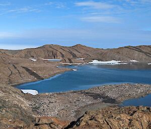 A rocky hilly landscape with a lake in the middle and a red hut in the distance set in the hills.