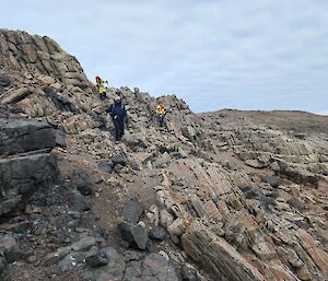 A group of three people wearing backpacks clambers over a rocky hillside.