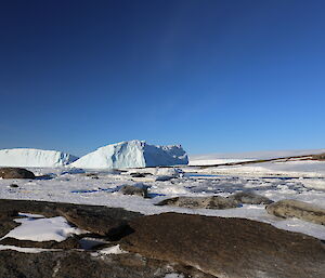 Looking across rock and ice with two icebergs in the distance