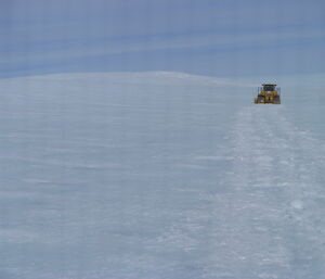 A yellow dozer is moving away across ice