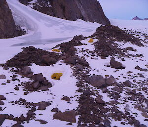 Three yellow bivvy bags lay amongst rock and ice