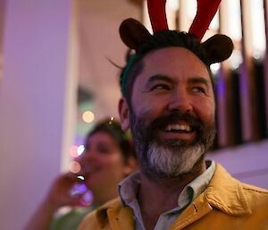 A man in a yellow short coat and reindeer antlers smiles