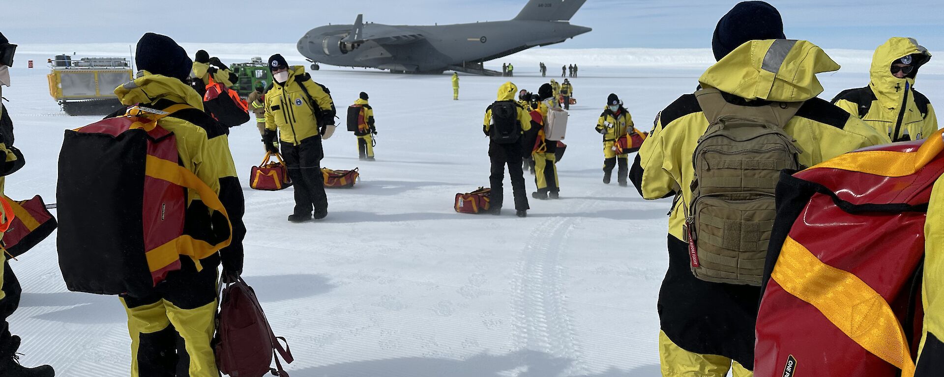 A crowd of people in Antarctic survival gear look on towards a C-17A in the background.