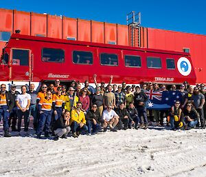 A large group of people in a range of summer and Antarctic clothing stand in front of the big red Terra Bus