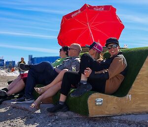 Four people sit on an outdoor chair looking like they are watching the cricket