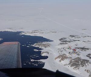 A photo from the air. The station is marked by colourful buildings in an expanse of snow and rock, with a plane wing in the foreground.