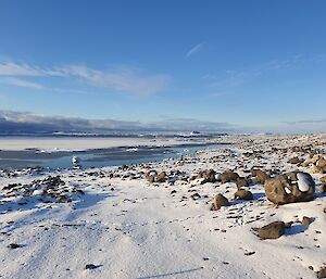 A rocky shoreline covered in snow. In the distanbce the sea has partially frozen and is also covered in a light dusting of snow. Clouds loom on the horizon.