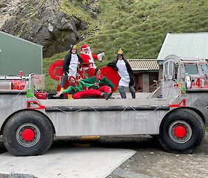 A group of people dressed as Christmas elves, Santa and a penguin on top of an amphibious vehicle