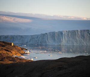 An ice cliff rises from the water in the distance