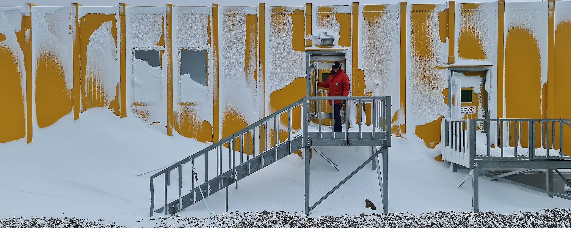 A man is at the door of a yellow building coated in windblown snow