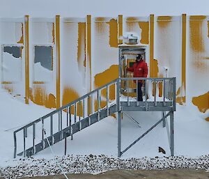 A man is at the door of a yellow building coated in windblown snow