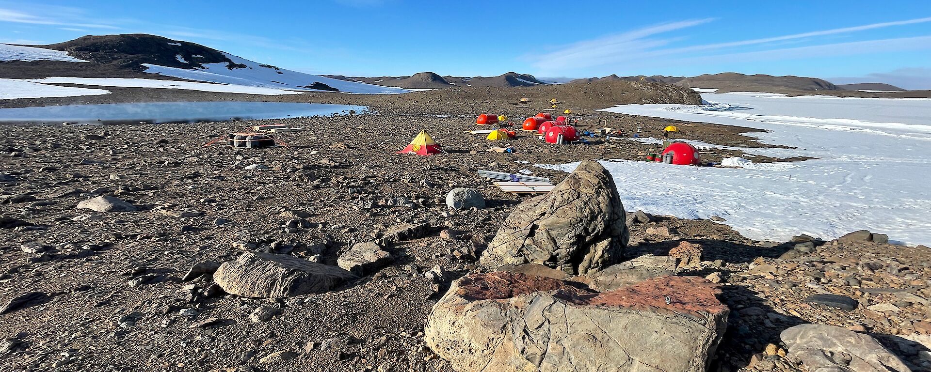 Tents set up among the rocks, surrounded by snow and blue skies