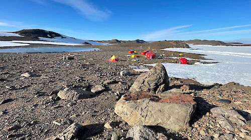 Tents set up among the rocks, surrounded by snow and blue skies