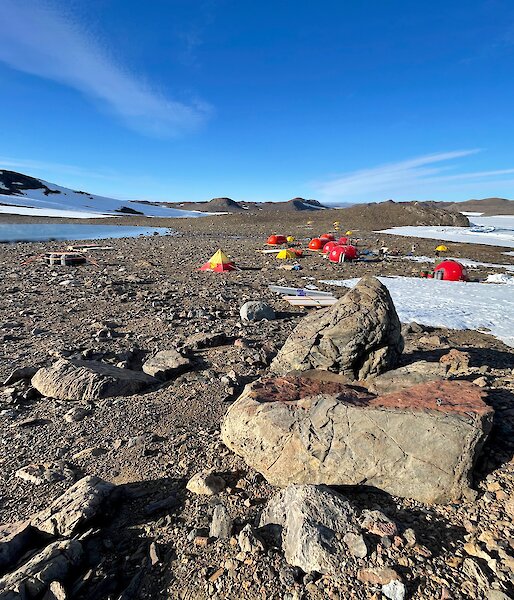 Tents set up among the rocks, surrounded by snow and blue skies