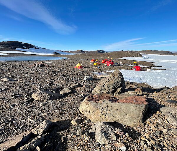 Tents set up among the rocks, surrounded by snow and blue skies